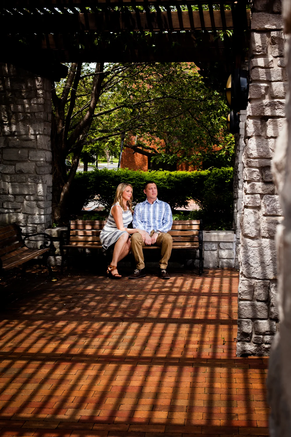 Bride and groom in shadows sitting on park bench.