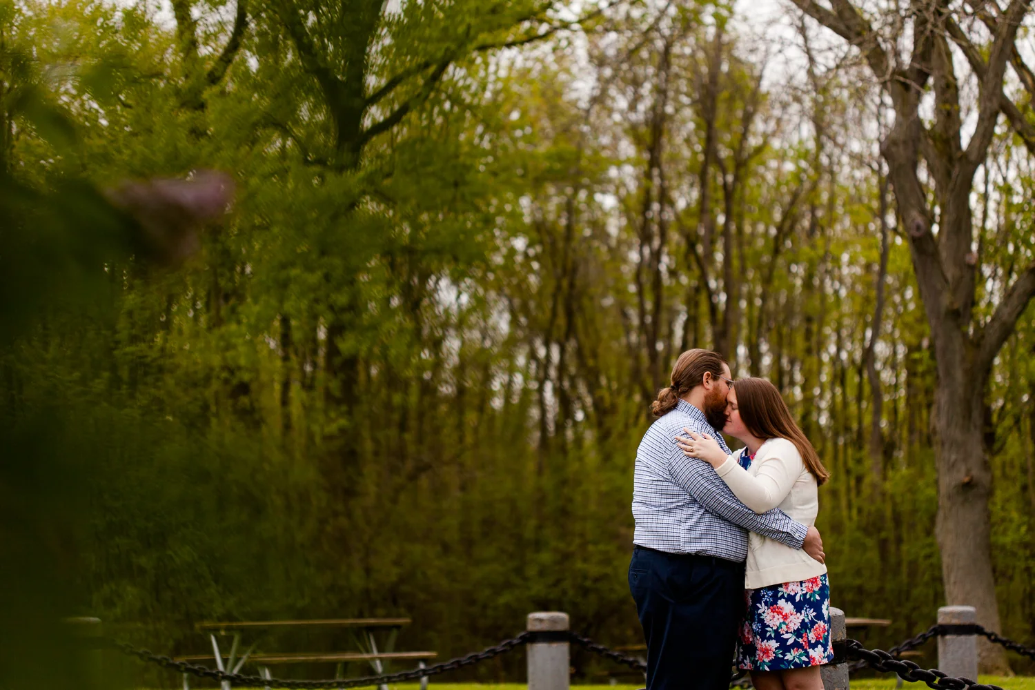 A sweet engagement photo of a woman in a blue floral dress and a man in a blue plaid shirt. They are at Onondaga Lake Park in Syracuse NY.