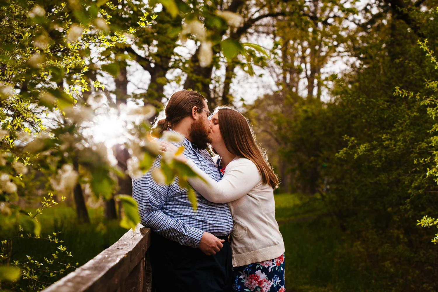 Girl kisses guy on a bridge while light shines through behind them.