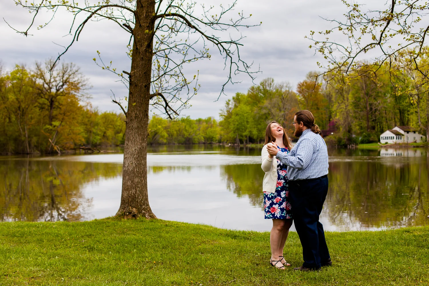 A couple dances in front of a lake. The woman is laughing.
