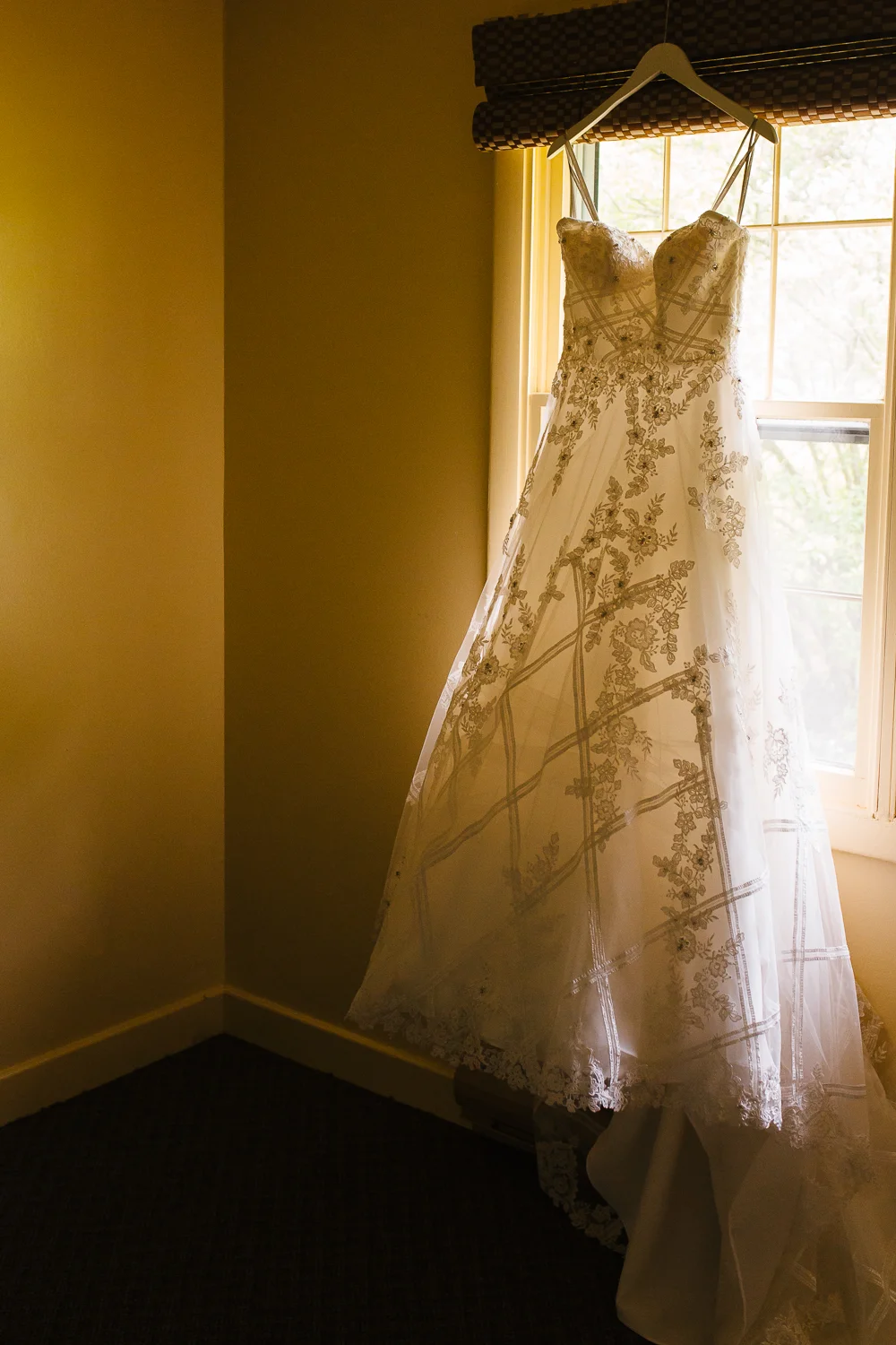 Full length wedding dress hangs in an empty room. The dress is white and lacey.