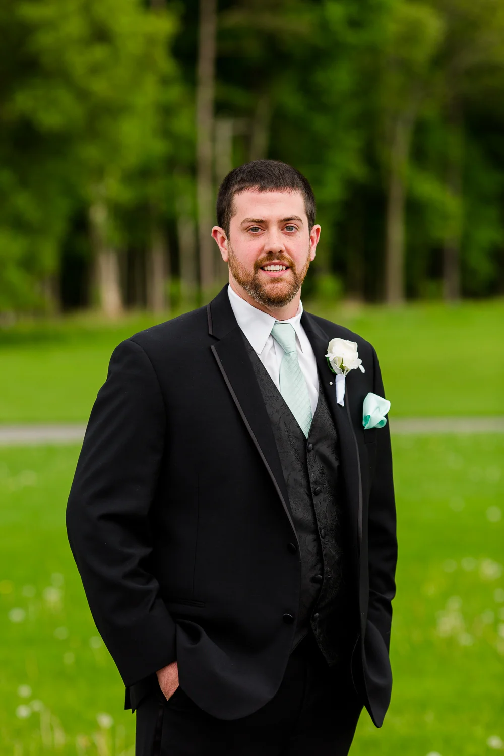 Portrait of a groom in a black tuxedo with a blue tie.