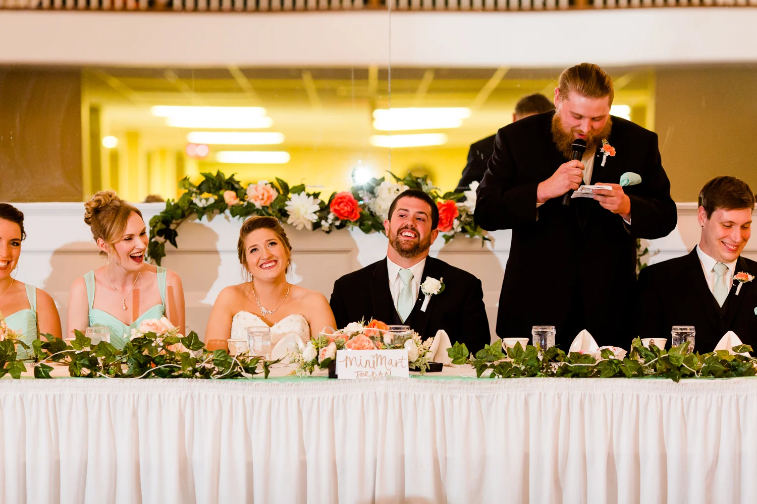 Best man gives a toast to the bride and the groom. The couple smiles. 