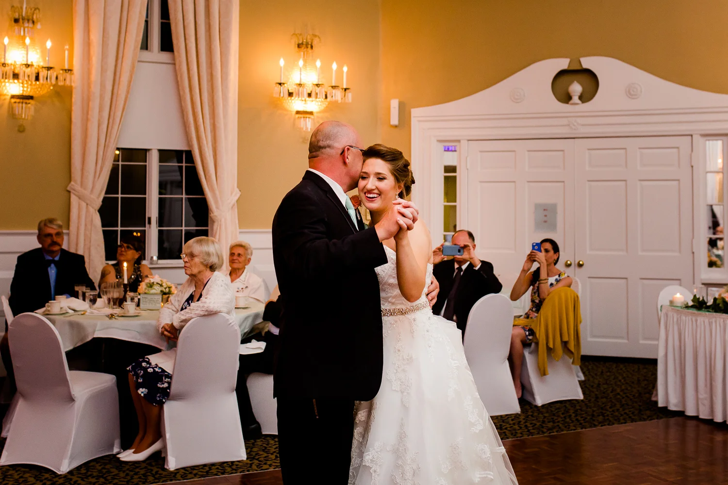 The bride and her father share a sweet moment during the father daughter dance at her wedding. The father kisses the side of her head while the bride smiles.