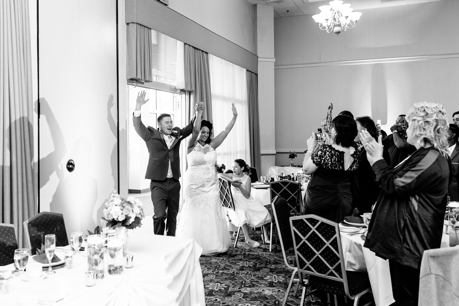  A black and white image of the bride and groom entering the reception. They have their hands up in the air. 