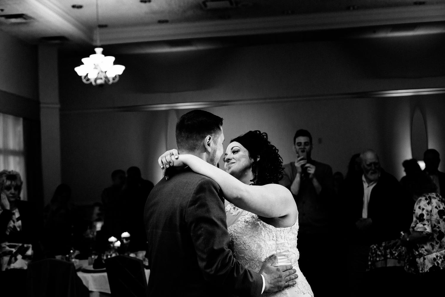  A black and white image of the first dance at a wedding. The bride is smiling at the groom. 