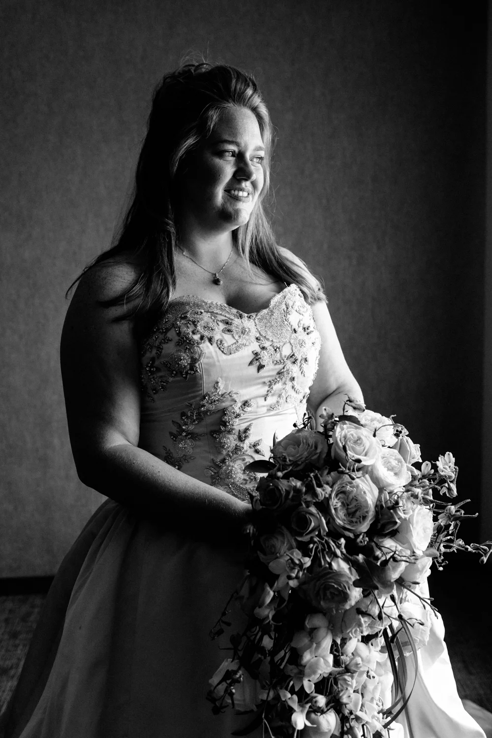 Black and white image of the bride holding her flowers. She looks out a window.