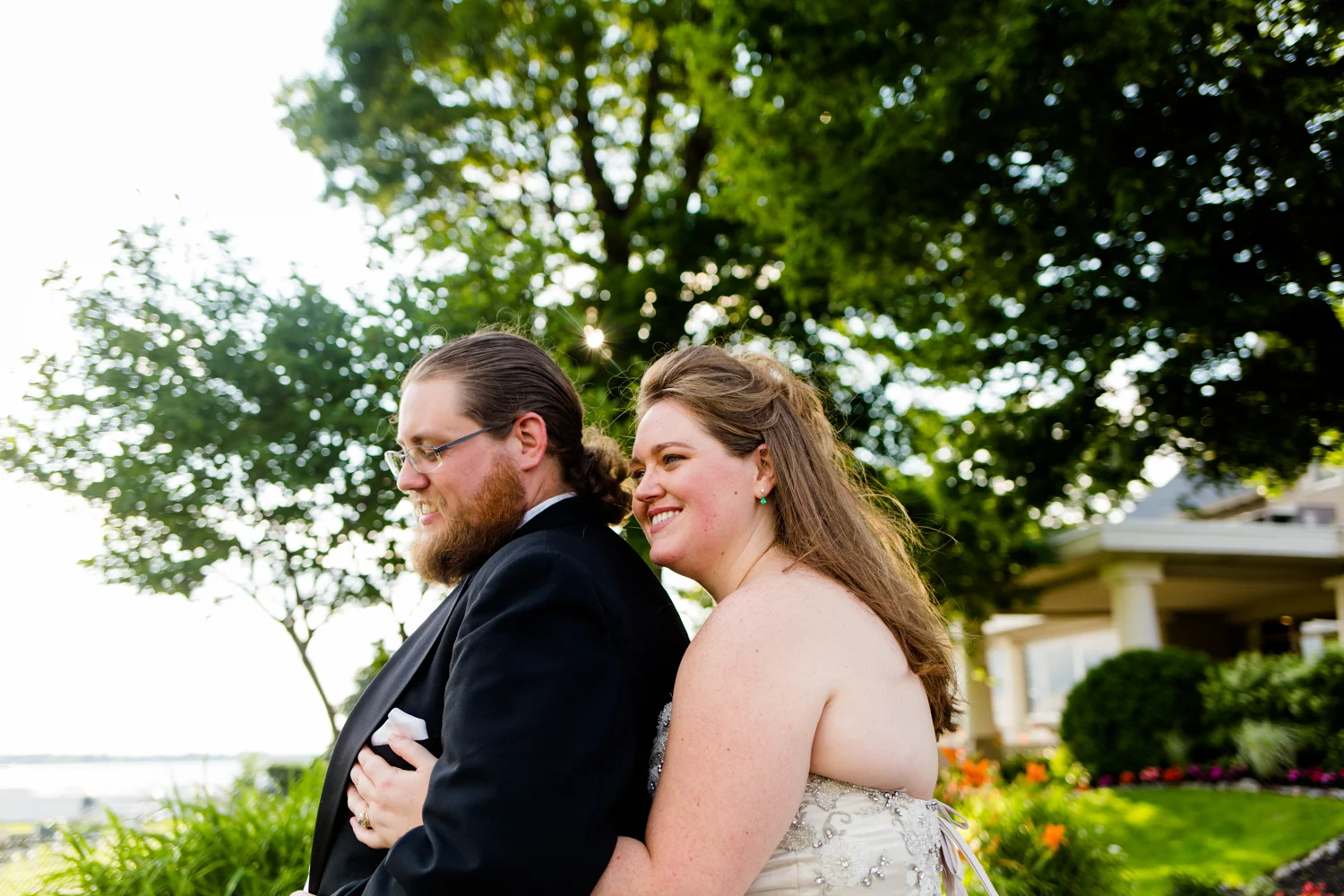 Portrait of bride hugging groom from behind. They are both smiling.