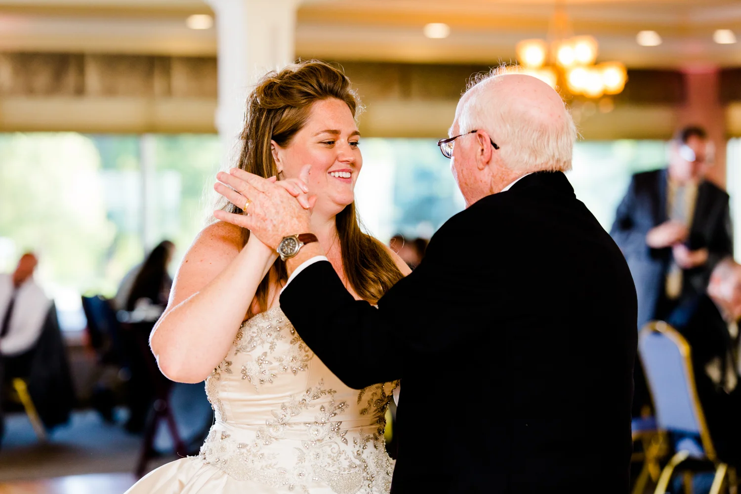 Bride smiles at her dad as they share a dance during her wedding reception.
