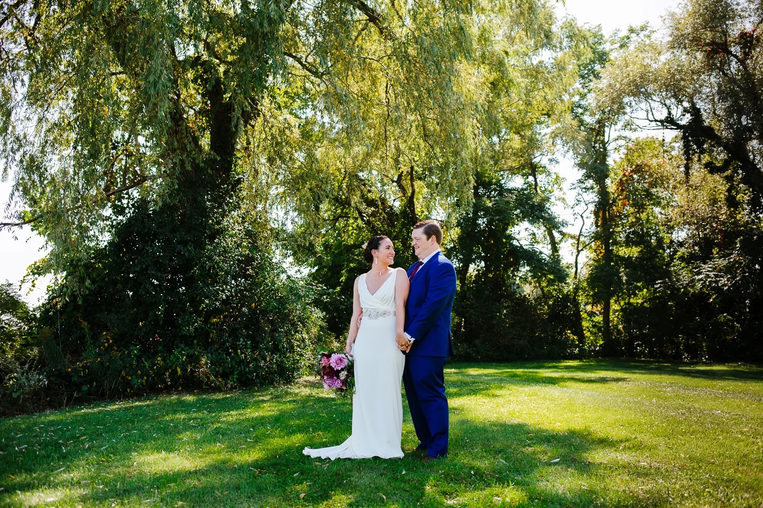 Bride and groom look at each other in front of a willow tree.