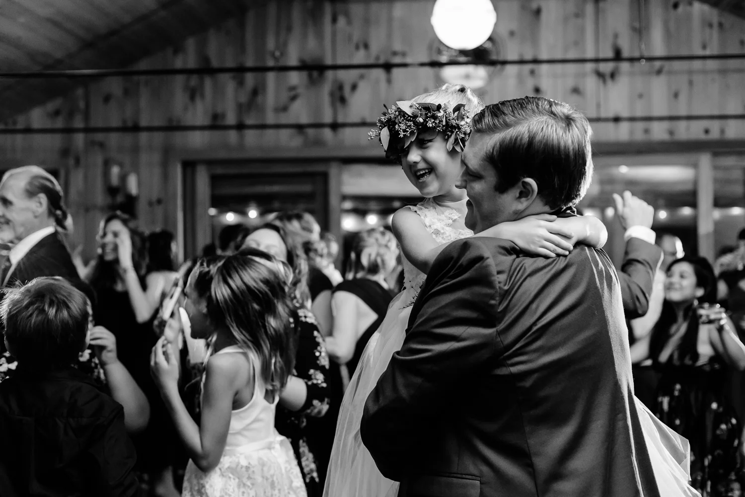 Black and white image of groom dancing with flower girl at a wedding reception.