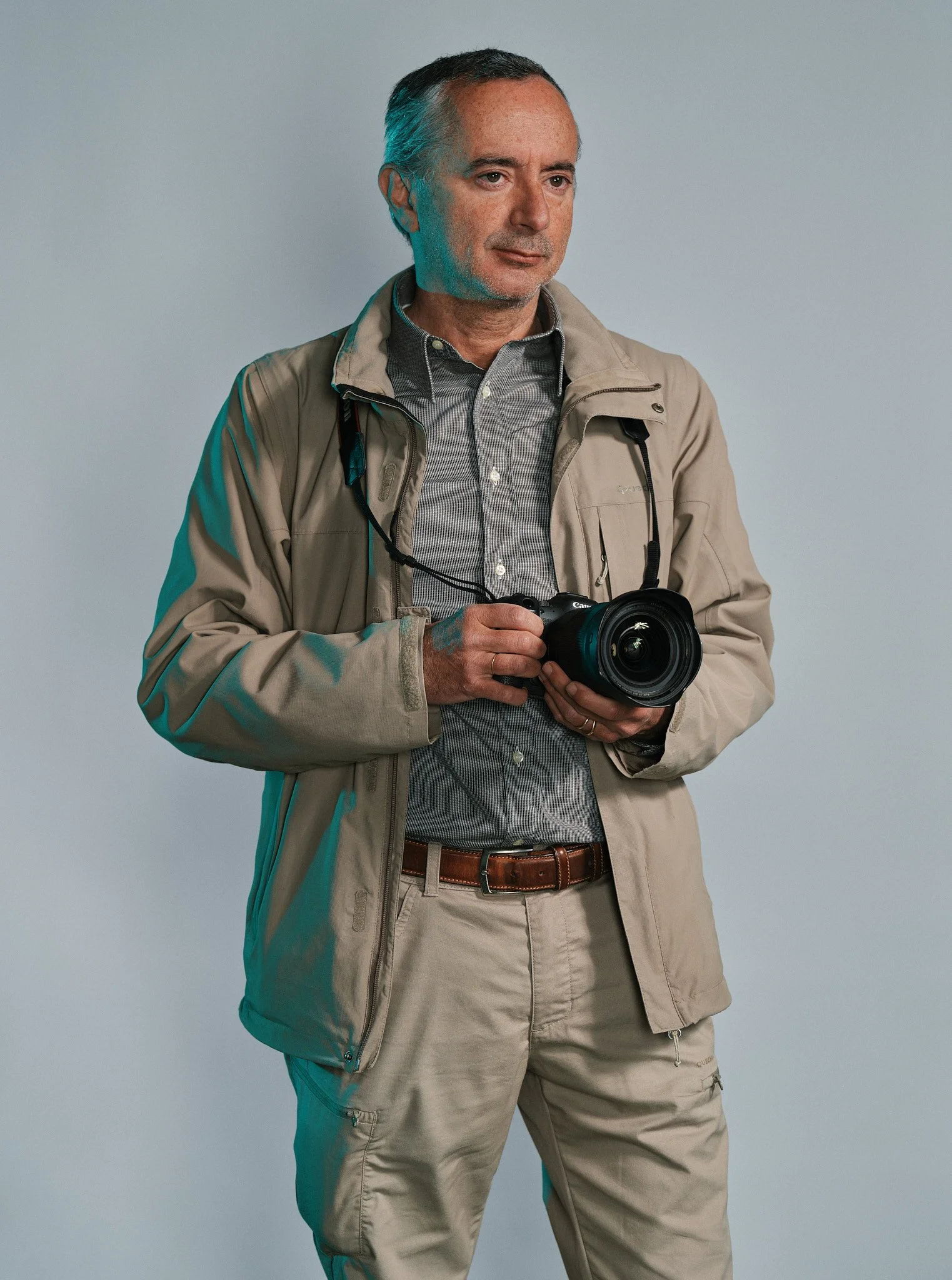 Un uomo d'etichette vestito con una camicia a maniche lunghe e una giacca beige, che tiene una fotocamera professionale con entrambe le mani.
