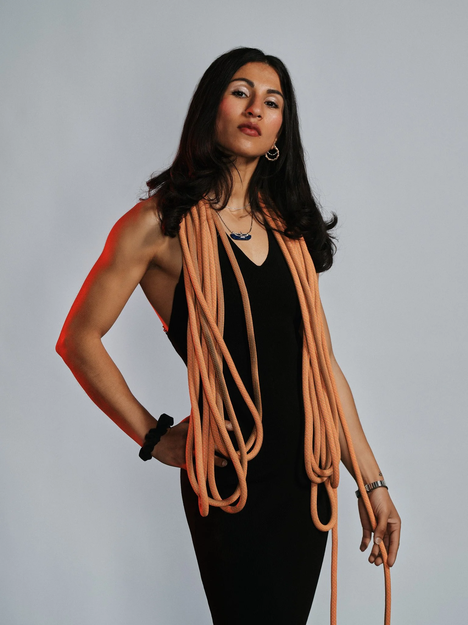 Donna con abito nero, orecchini e collana, avvolta in una corda arancione.