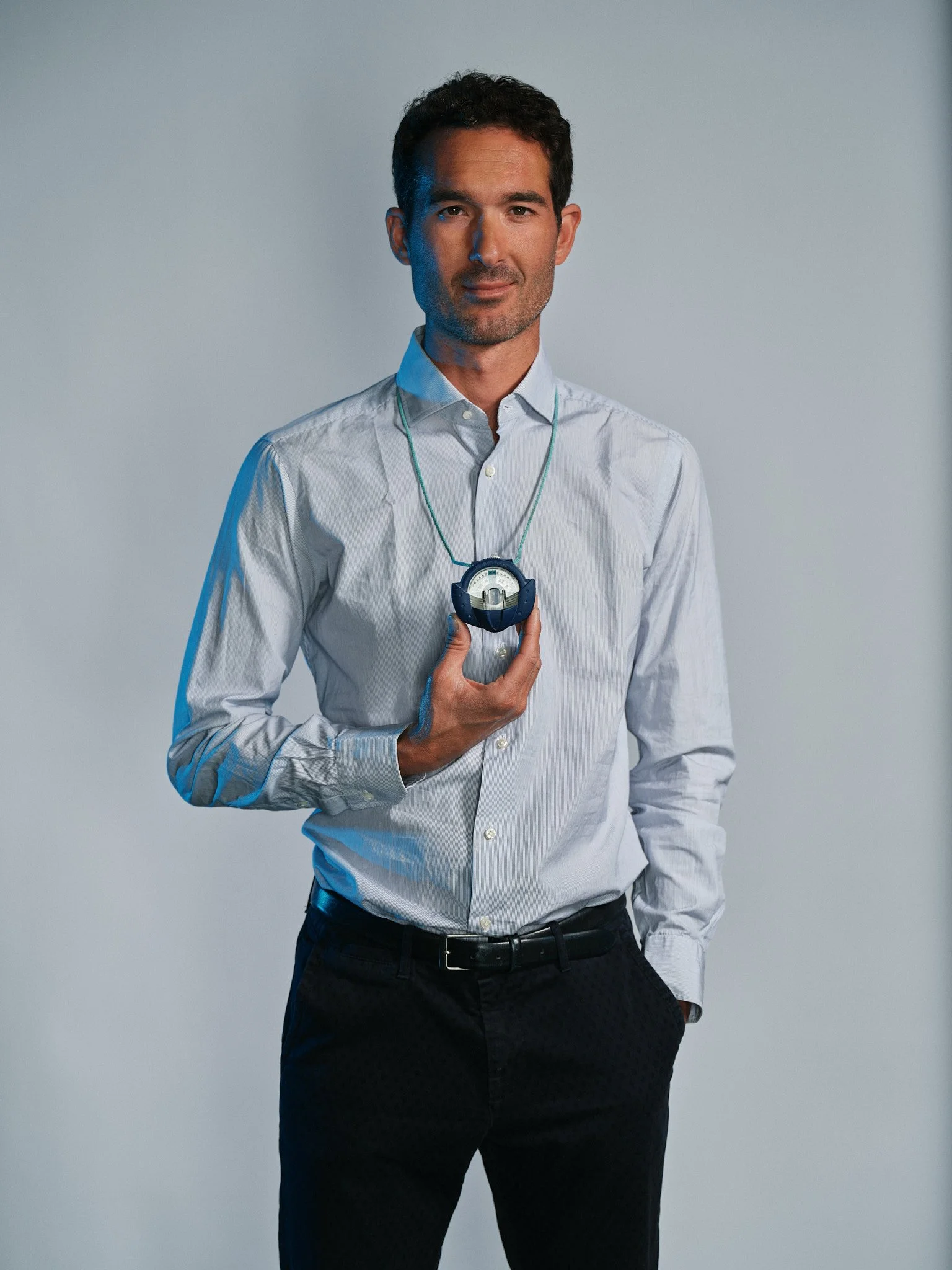 Uomo in camicia bianca che tiene in mano un orologio digitale attorno al collo, sfondo neutro