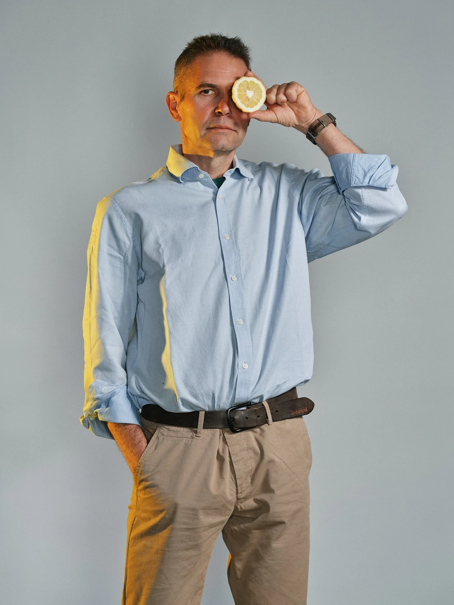 Uomo con camicia azzurra che tiene un limone davanti all'occhio destro