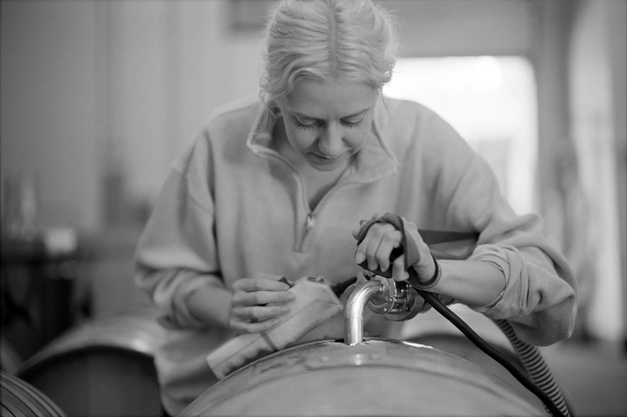 Black and white photo of a woman barreling down wine in a barrel.