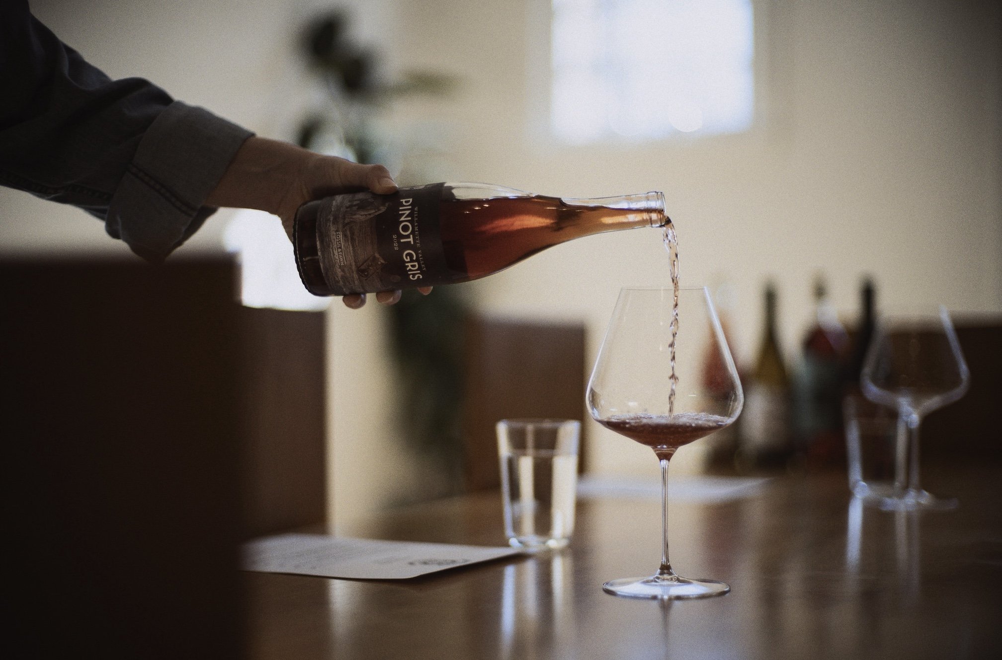 Person pouring red wine from a bottle of our Willamette Valley Pinot Gris into a wine glass on a table.