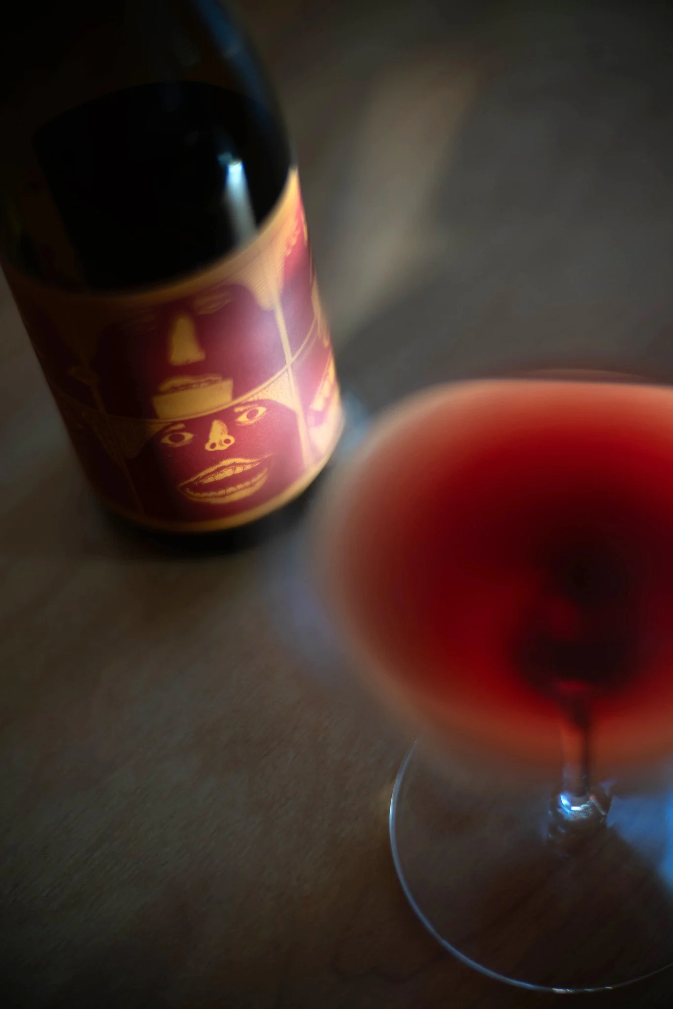 A bottle of our Willamette Valley Pinot Noir and a wine glass filled on a wooden table, with sunlight casting shadows in the background.