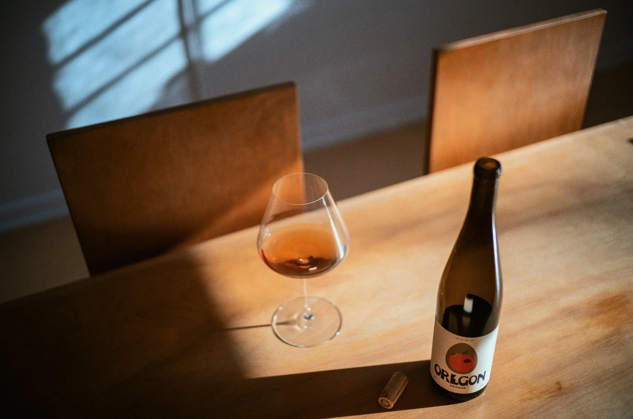 A wooden dining table with a glass of our Oregon orange wine.