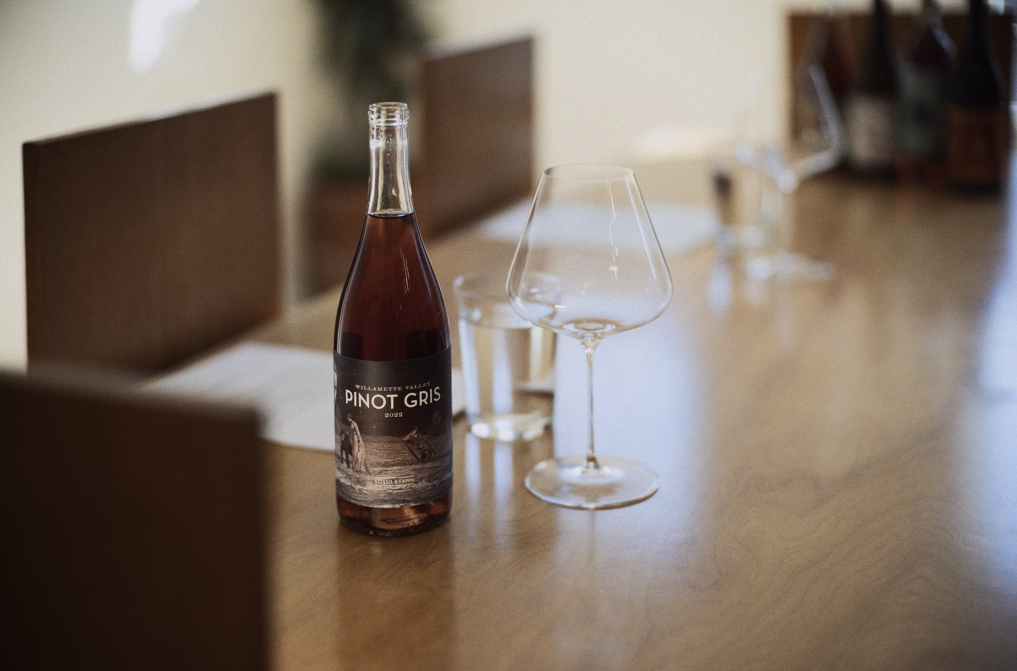 A bottle of Willamette Valley Pinot Gris wine with two empty wine glasses and a glass of white wine on a wooden table in a dining room.