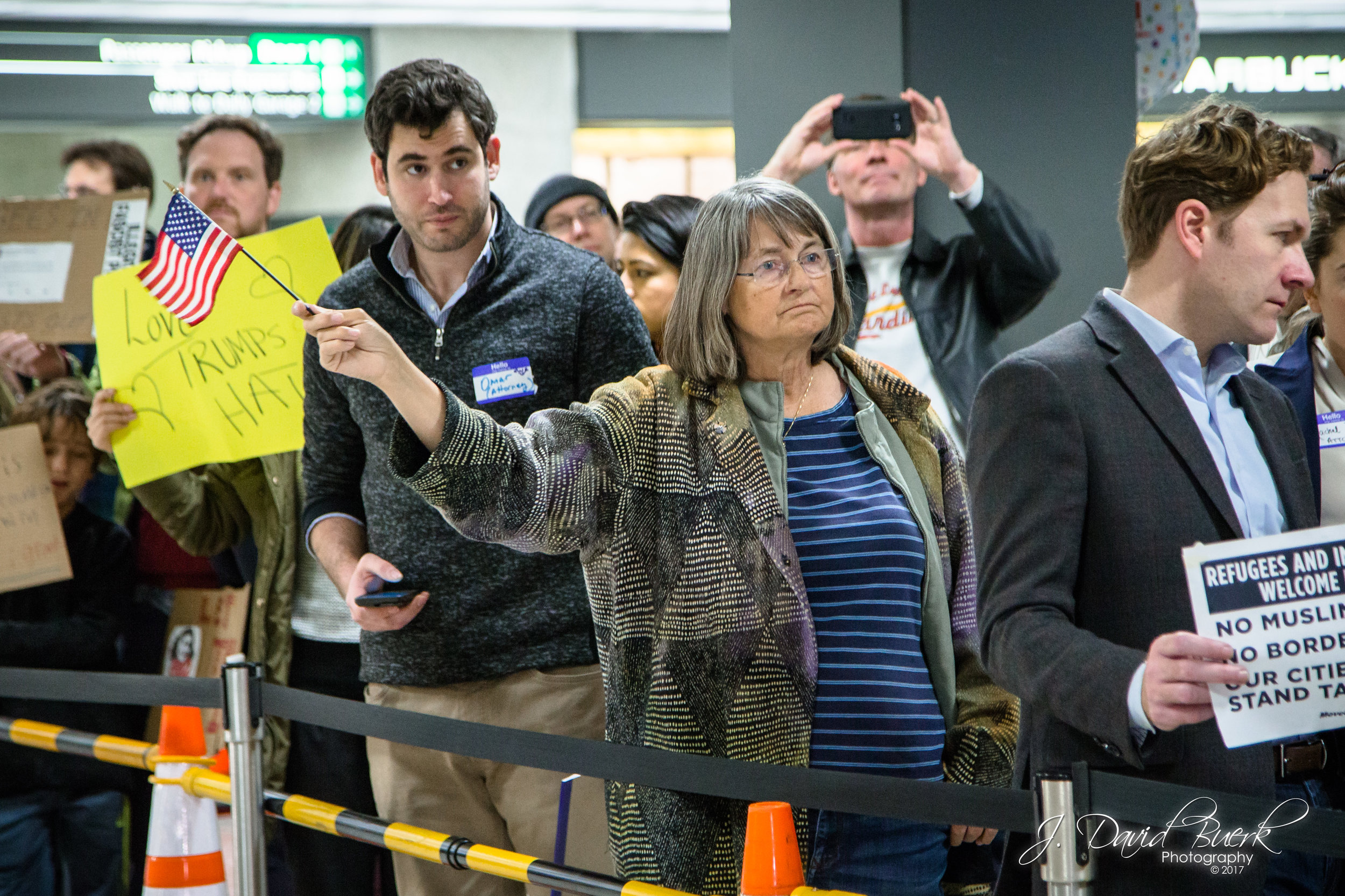 A woman waves an American flag as arriving international passengers are greeted by the crowd of protestors.