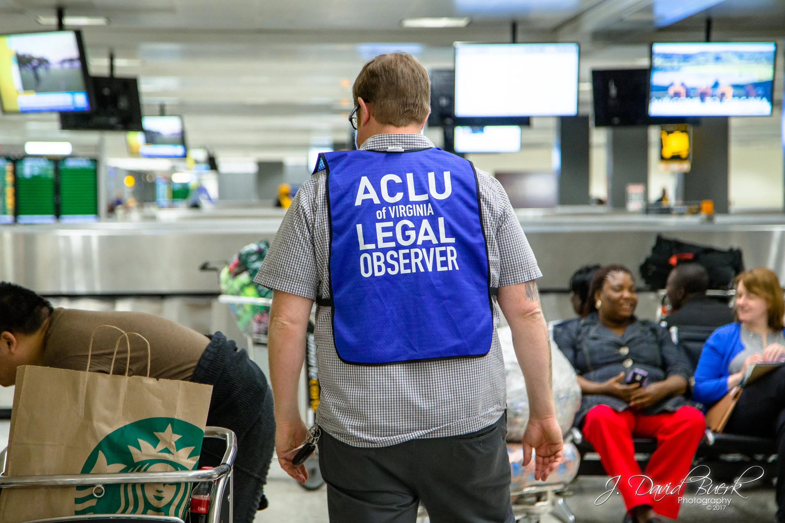 An American Civil Liberties Union legal observer in a blue high-visibility vest. When news of the travel ban broke on Saturday, lawyers, translators, and legal observers converged upon airports to donate their time and efforts in investigating and protecting against civil liberty violations. The ACLU was quick to file a lawsuit in opposition to the executive order, resulting in an emergency stay granted by Brooklyn Federal Judge Ann Donnelly late Saturday night, which allowed travelers caught in the ban's rapid rollout to be released from detention.