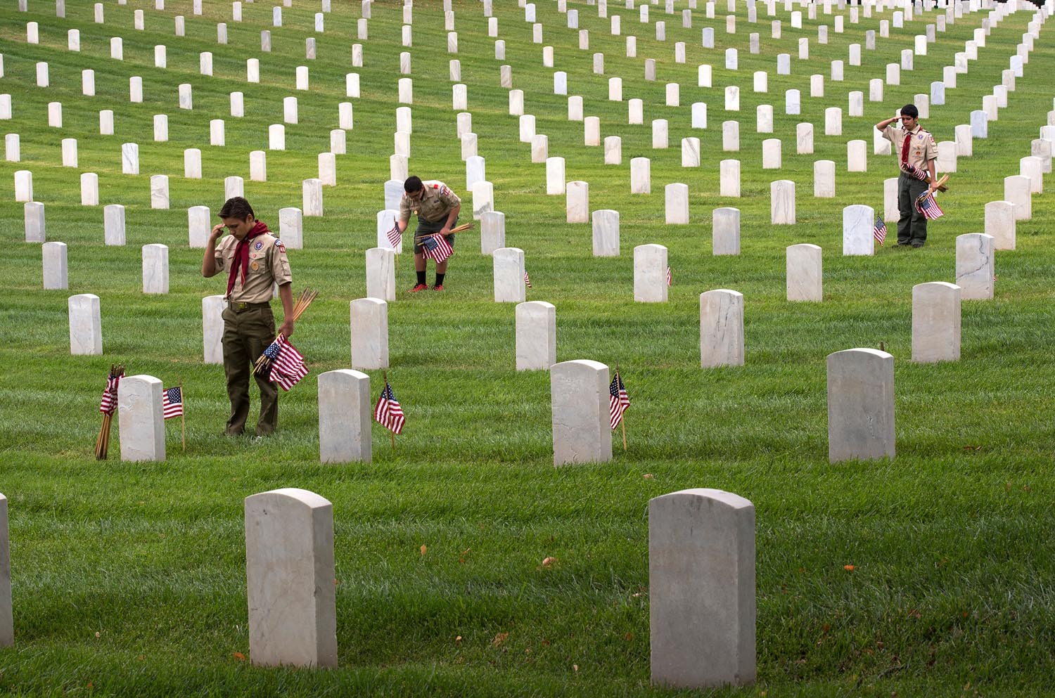 From left, Boy Scouts Troop 400, Dakota Hansen, 14, Christian Pinn, 14, and Kenny Grijalva, 15, place American flags, say the names and render salutes at the Los Angeles National Cemetery on Saturday. Hundreds of L.A. area Boy Scouts, Girls Scouts, Sea Cadets and others place American flags on each grave of over 88,000 war veterans.
