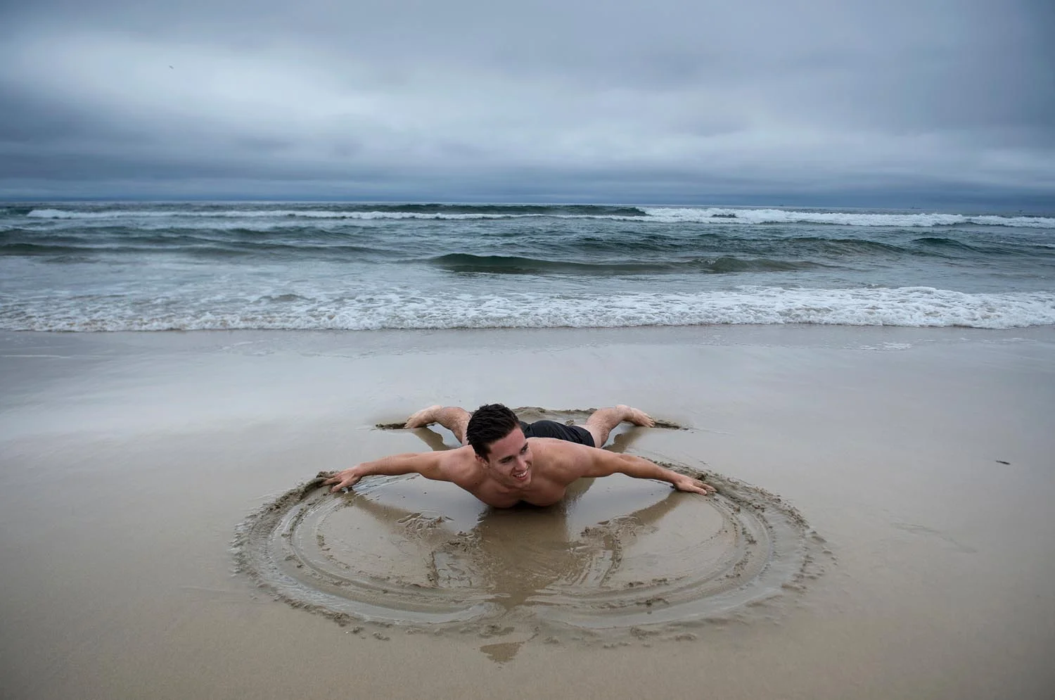 Richard Hardley, of New Zealand, makes a sand angel as his brother John Hardley takes a photo at Huntington State Beach on Wednesday. The two brothers are on vacation. They said we arrived the day it started to rain, we may have brought the rain from New Zealand jokingly. Richard Hardley is all smiles as he says the rain is not going to stop me from swimming in Huntington Beach.