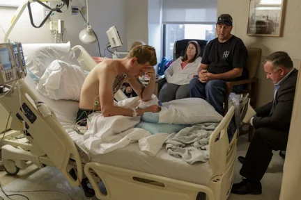 Vegan Activist Brad Bethell sits with his parents and a family attorney in his room at Cedars Sinai Hospital in Beverly Hills, an area in the city of Los Angeles, CA, shortly after being admitted to the hospital with several broken ribs, a broken jaw and nose, and serious internal bleeding from being assaulted 24 hours previously by a bouncer at local Venice Beach bar 'The Other Room'. Brad was showing the bar's patrons a slide show of animal abuse on a laptop thrust into their view from the street outside the bar, an action which angered security. Brad has no health insurance and is homeless: his impending surgeries are adding onto an ever increasing medical bill he does not know how to pay. Photo by Ruth Iorio on May 7th 2017 (Santa Monica College, Photo 13 Spring 2017, Gerard Burkhart)