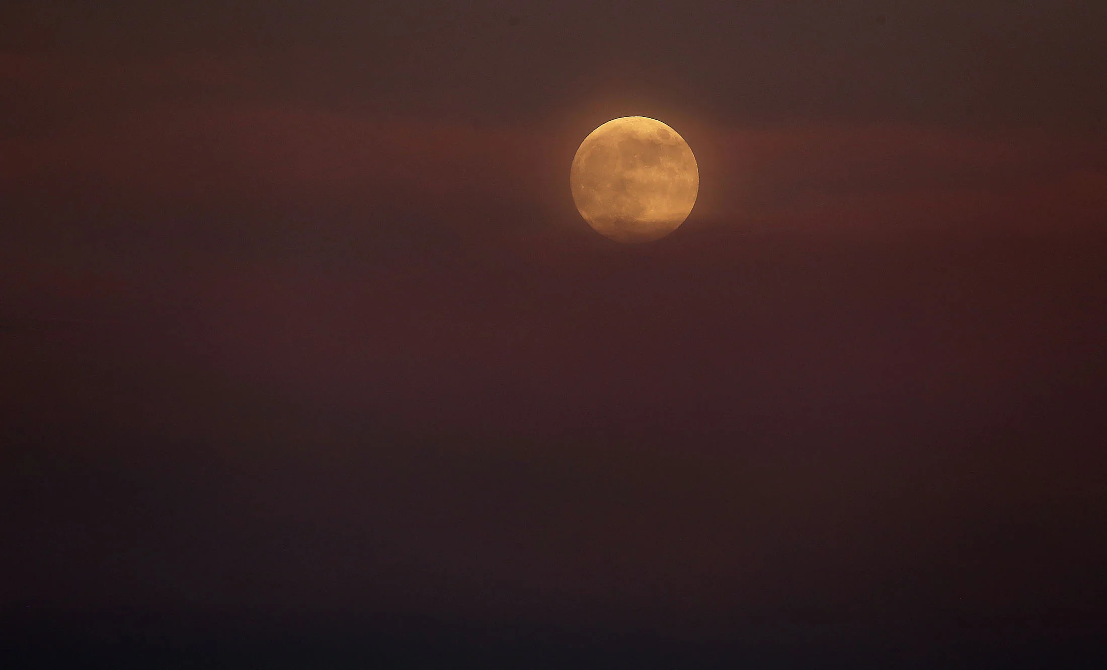 The full moon rises in the colorful smoke from the Cranston fire in the San Bernardino National Forest above Lake Hemet on Thursday, July 26, 2018.