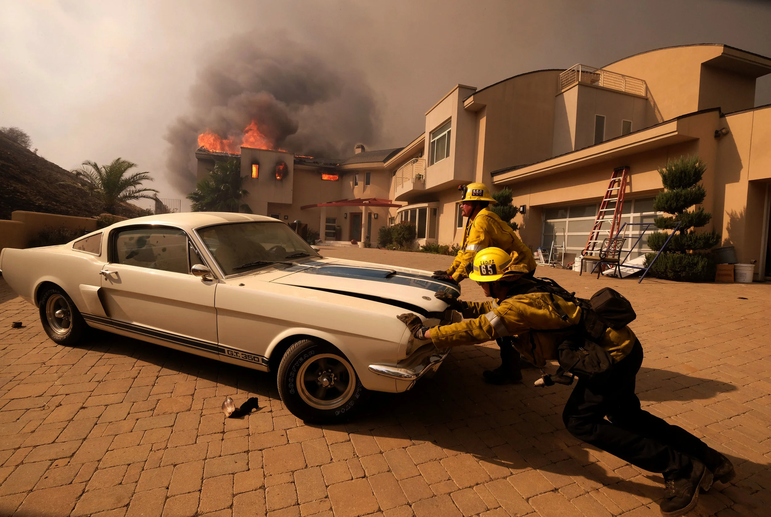  Firefighters push a vehicle from a garage as the Woolsy fire burning a home near Malibu Lake in Malibu, Calif., Friday, Nov. 9, 2018.  