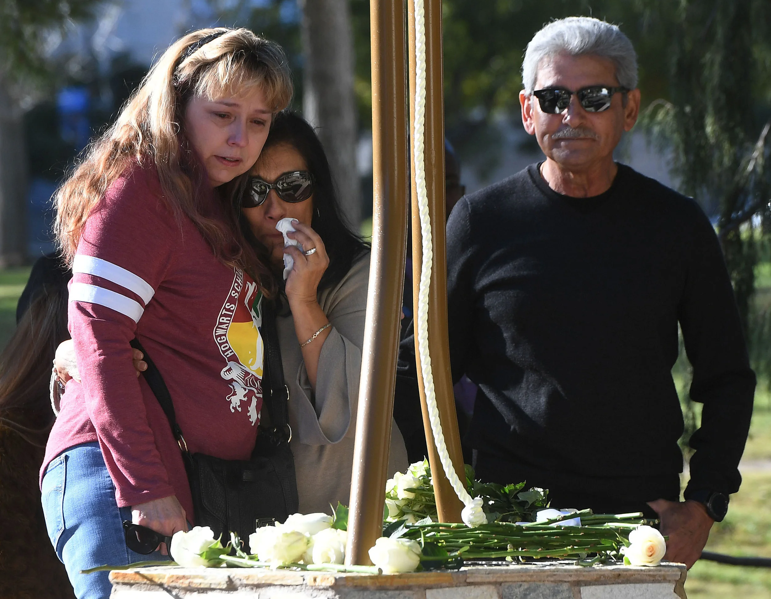  Robert Velasco (right), whose daughter Yvette was killed in the Inland Regional Center mass shooting, stands next to a memorial on the Cal State San Bernardino campus as his wife Mari (center) hugs one of Yvette's coworkers and survivors (left), who