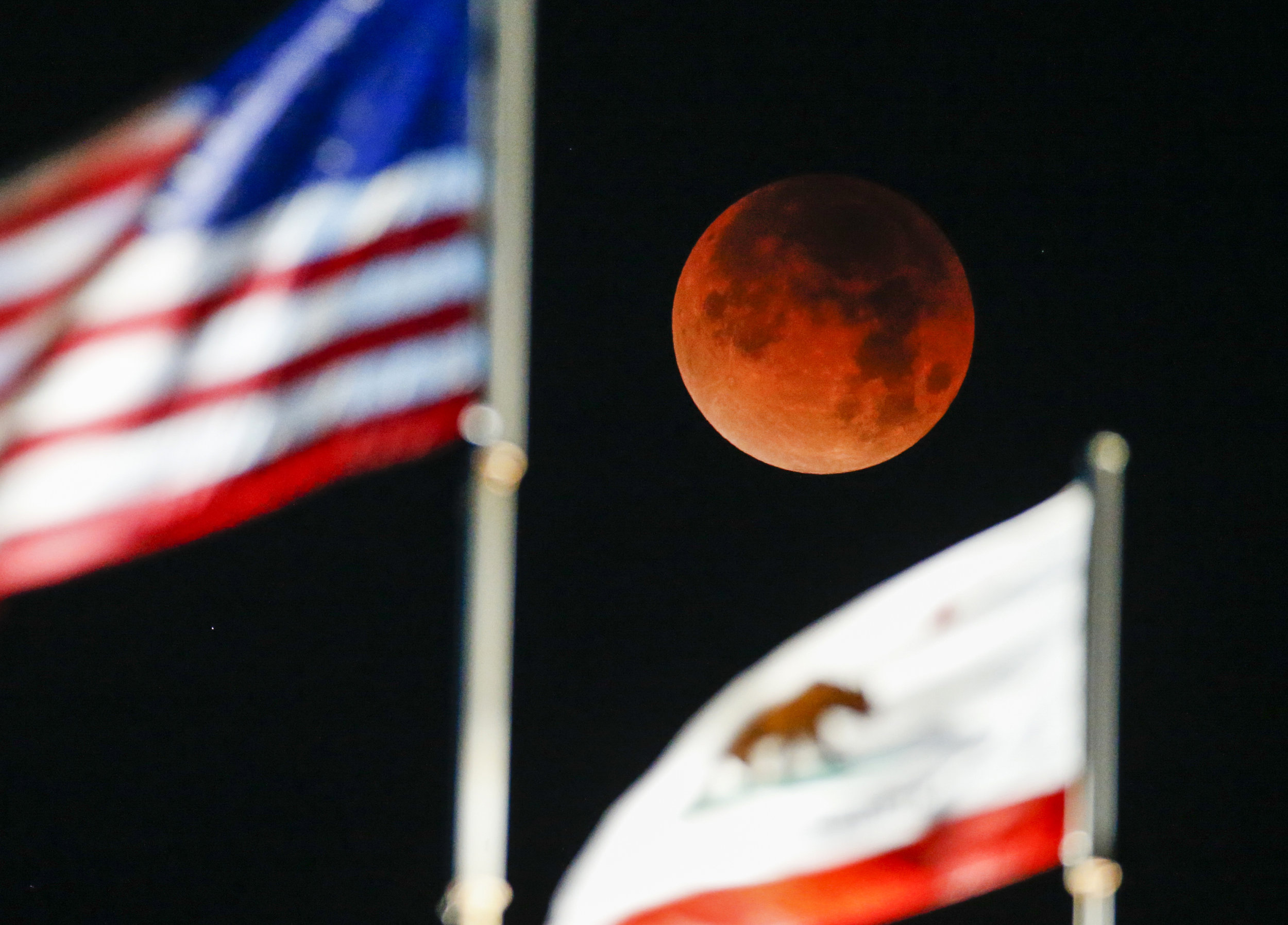  A rare celestial occurrence called a 'Super Blue Blood Moon' is seen behind the flags of U.S. and California State at Santa Monica Beach in Santa Monica, California, Wednesday, Jan. 31, 2018. 