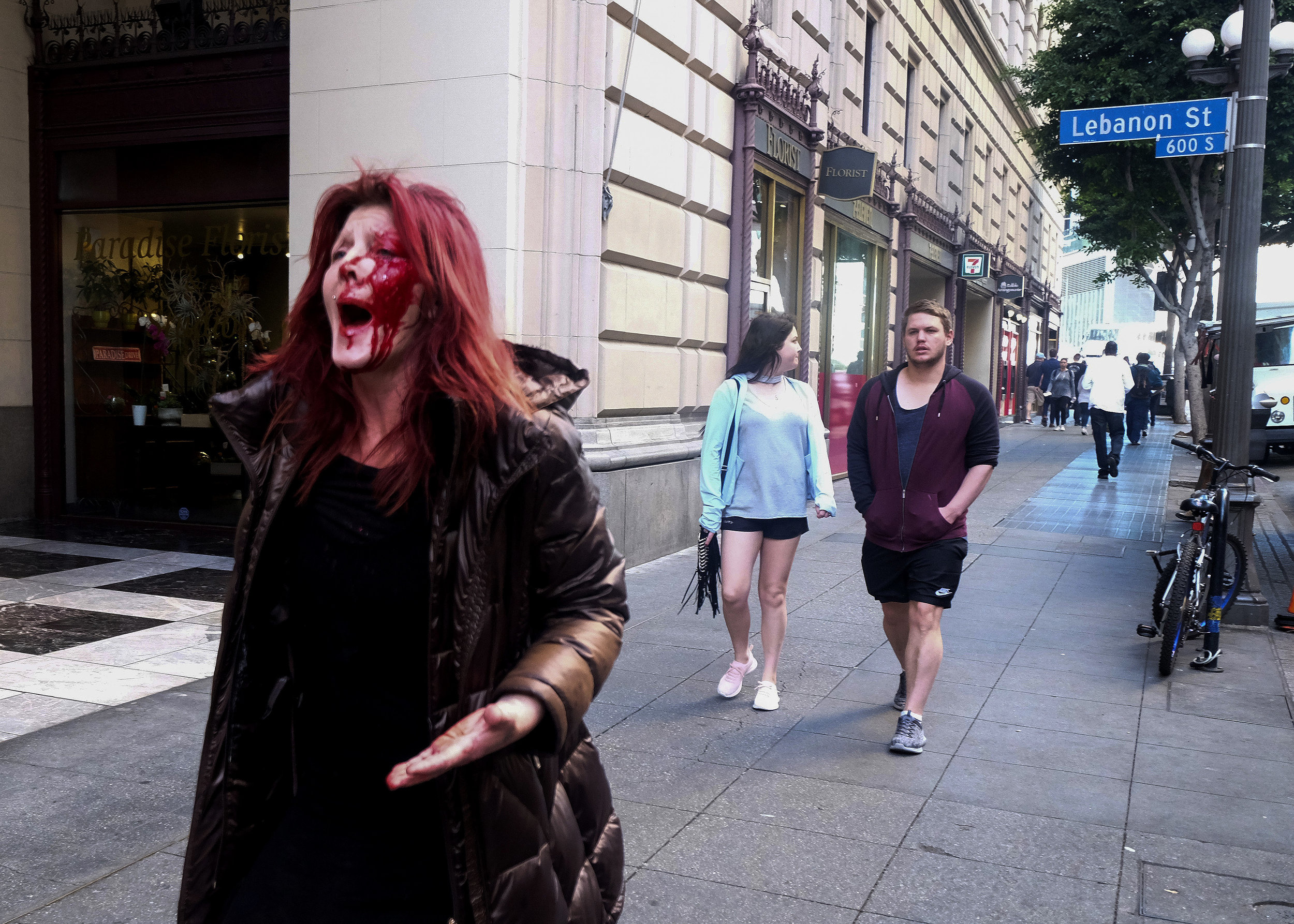  A woman with her face covered in blood after being assaulted by a man (white top in the back) in downtown Los Angeles, Wednesday, Jan 24, 2018. The suspect was taken into custody and it is believed he and the victim knew each other so this was not a