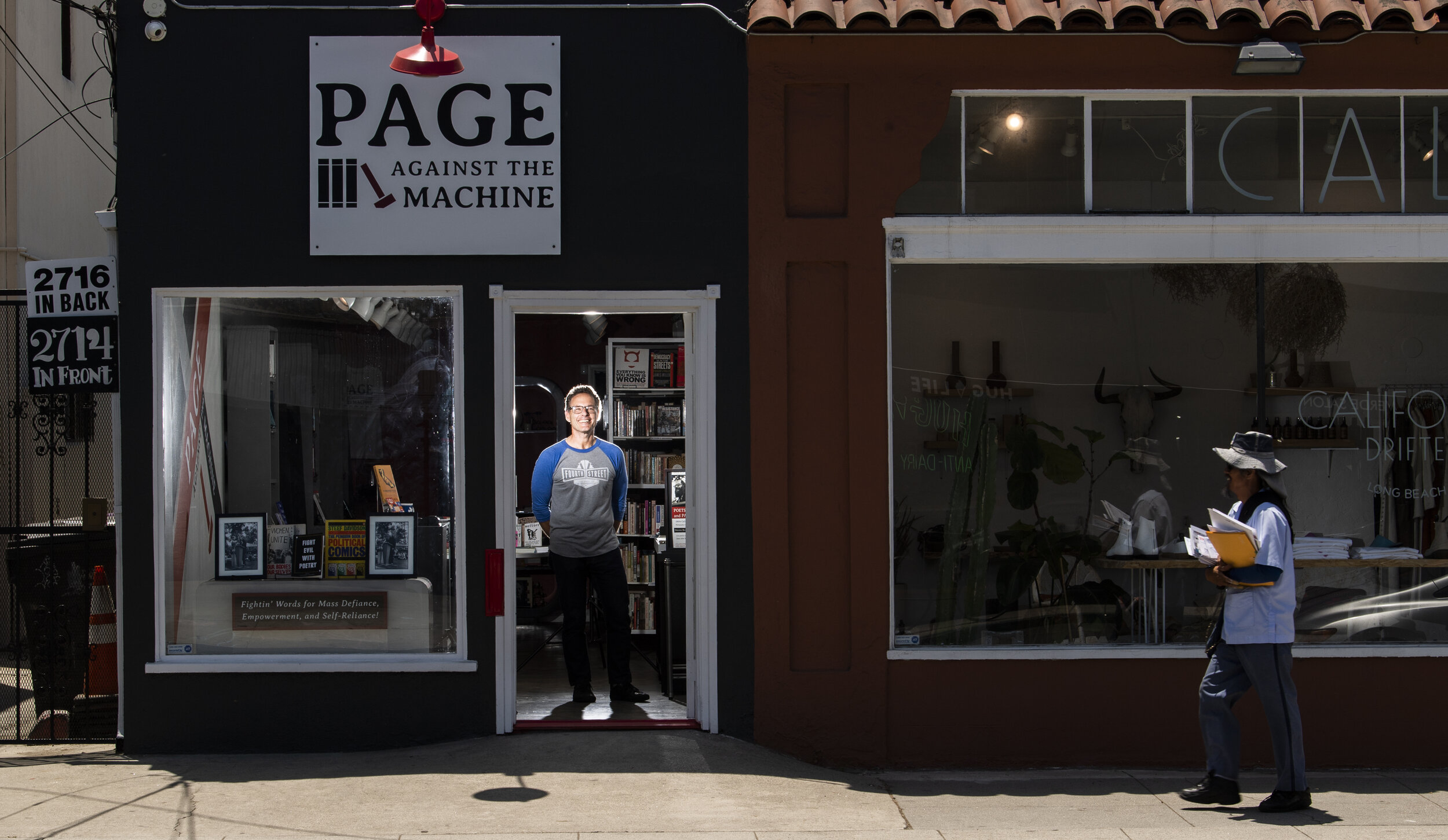 A mailman walks past the Page Against the Machine bookstore as Chris Giaco, owner, stands in the doorway of the new bookstore in Long Beach Thursday, July 11, 2019. Photo by Thomas Cordova. 
