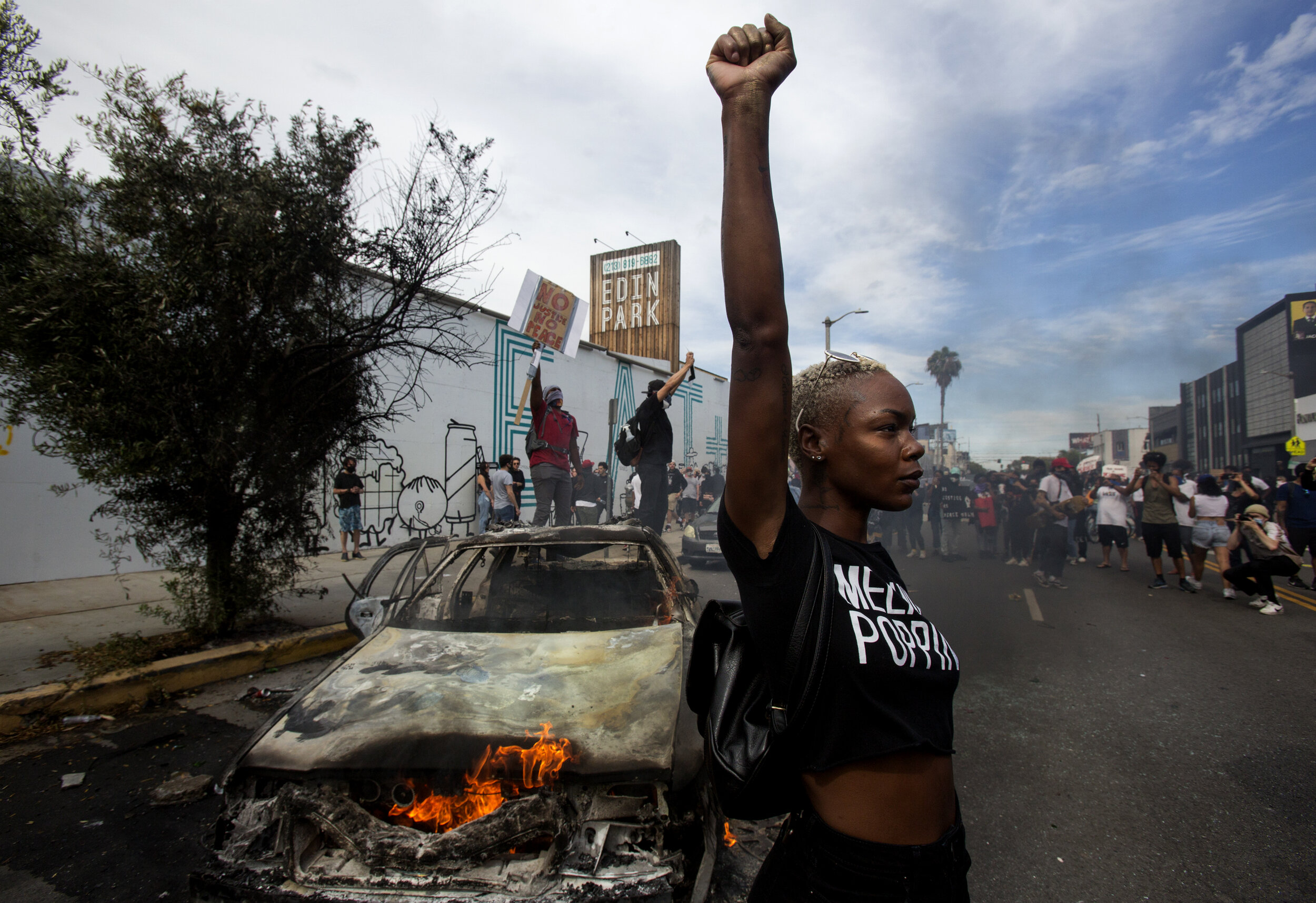  A protester raising her fist poses for photos next to a burning police vehicle during a protest over the death of George Floyd, a handcuffed black man in police custody in Minneapolis, in Los Angeles, Saturday, May 30, 2020.The 2020 Black Lives Matt