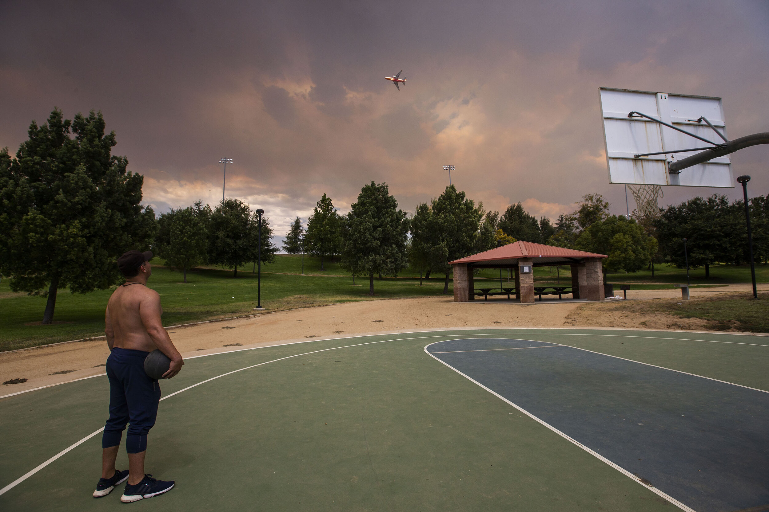  A basketball player stops shooting hoops at Yucaipa Community Park to watch as a DC-10 tanker flies over head to make a retardant drop on the El Dorado Fire as it burns close to homes in triple digit heat, wind gusts and low visibility in Yucaipa on