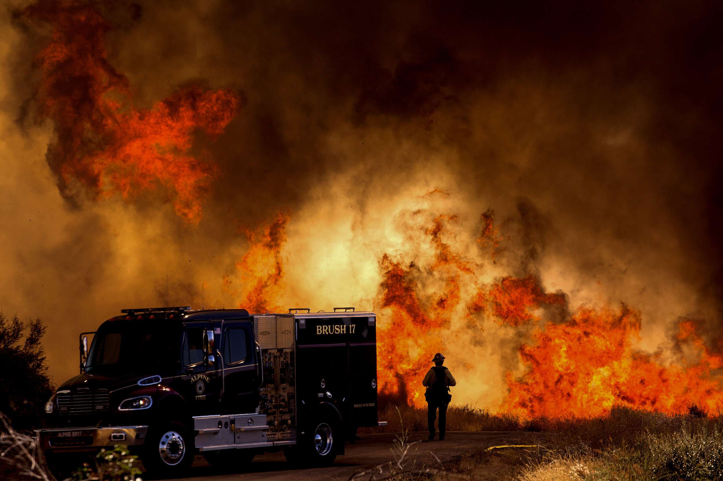  A firefighter stands next to a fire truck as flames from a brush fire flare at the Apple Fire in Cherry Valley, Calif., Saturday, Aug. 1, 2020. The 2020 California wildfire season was characterized by a record-setting year of wildfires that burned a