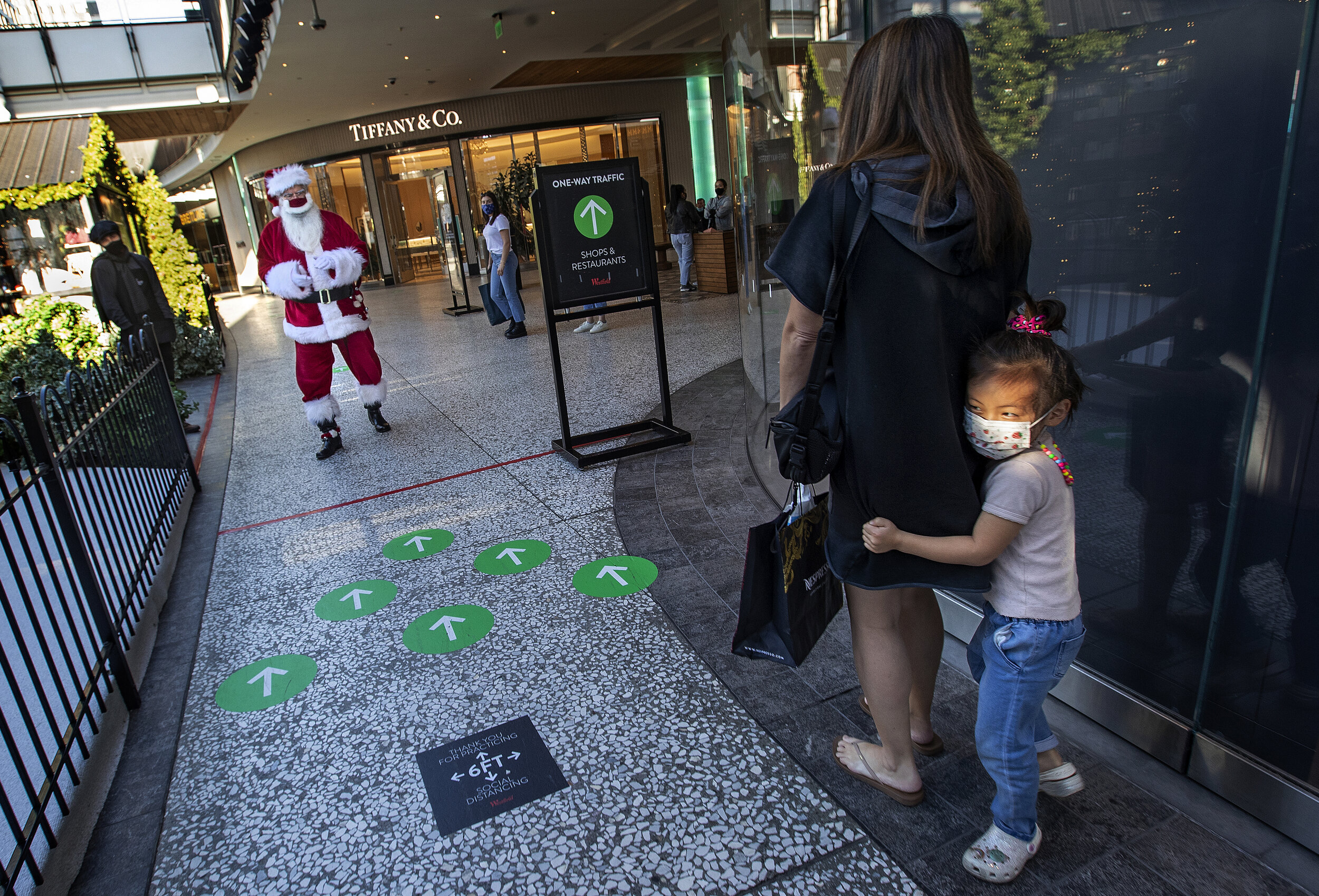  CENTURY CITY, CA - DECEMBER 03, 2020: Aerin Kim, 4, acting a little shy, hides behind her mom, Gina, after spotting Santa Claus (Larry Buckelew), at the Westfield Century City shopping mall. Santa was on his way to a lunch break. They are all wearin