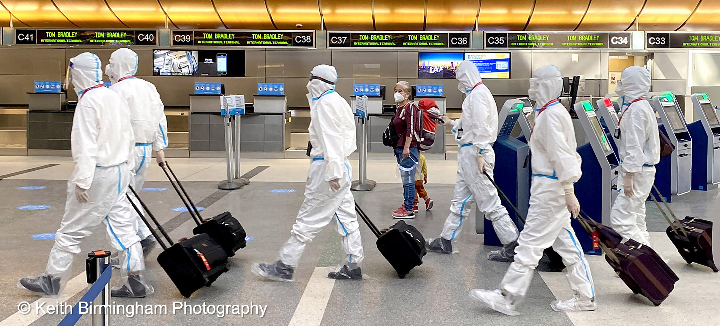  A woman with a child wearing masks looks on as an airline crew wearing full personal protective equipment due to the Coronavirus Pandemic walks through the Tom Bradley International Terminal at LAX in Los Angeles on Tuesday, November 17, 2020. (Phot
