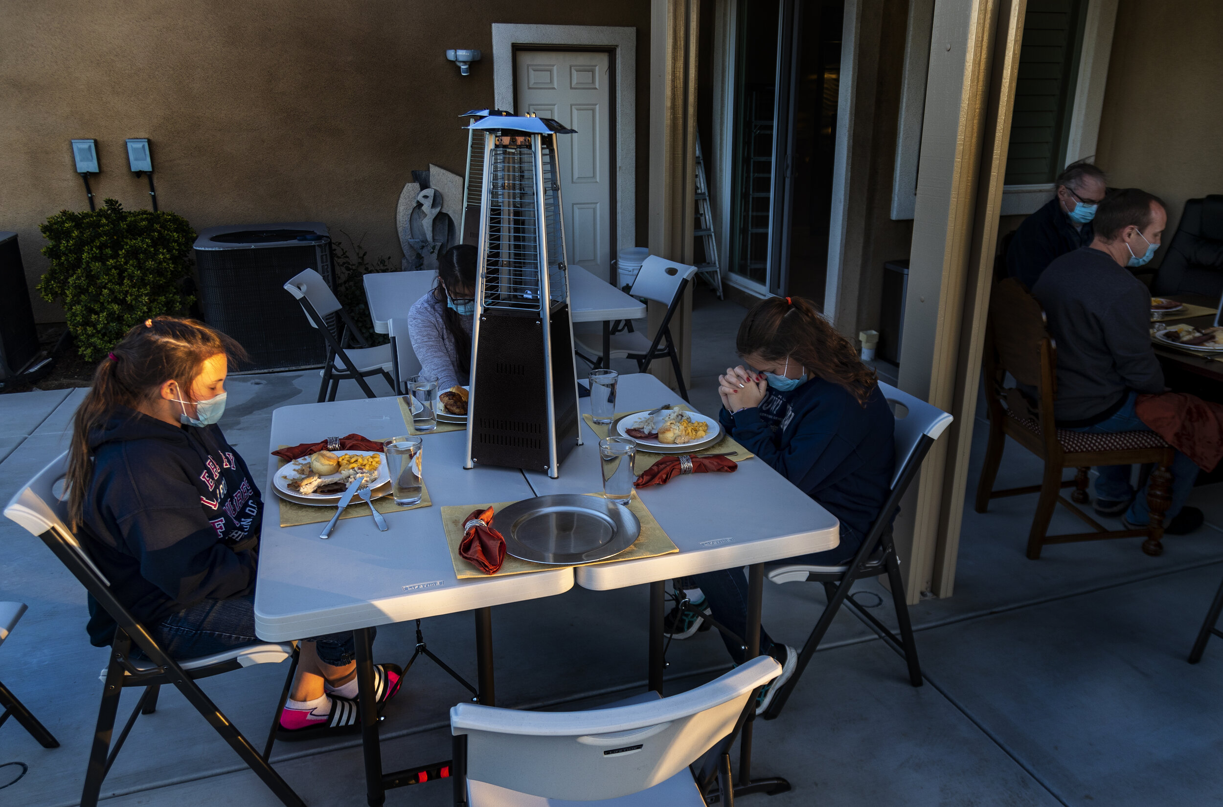  RIVERSIDE, CA - NOVEMBER 26, 2020:  Wearing a mask Dalilah Stoye,13, left, leads the family in a blessing before eating their Thanksgiving feast on November 26, 2020 in Riverside, California. Despite windy conditions, the families still ate outside 