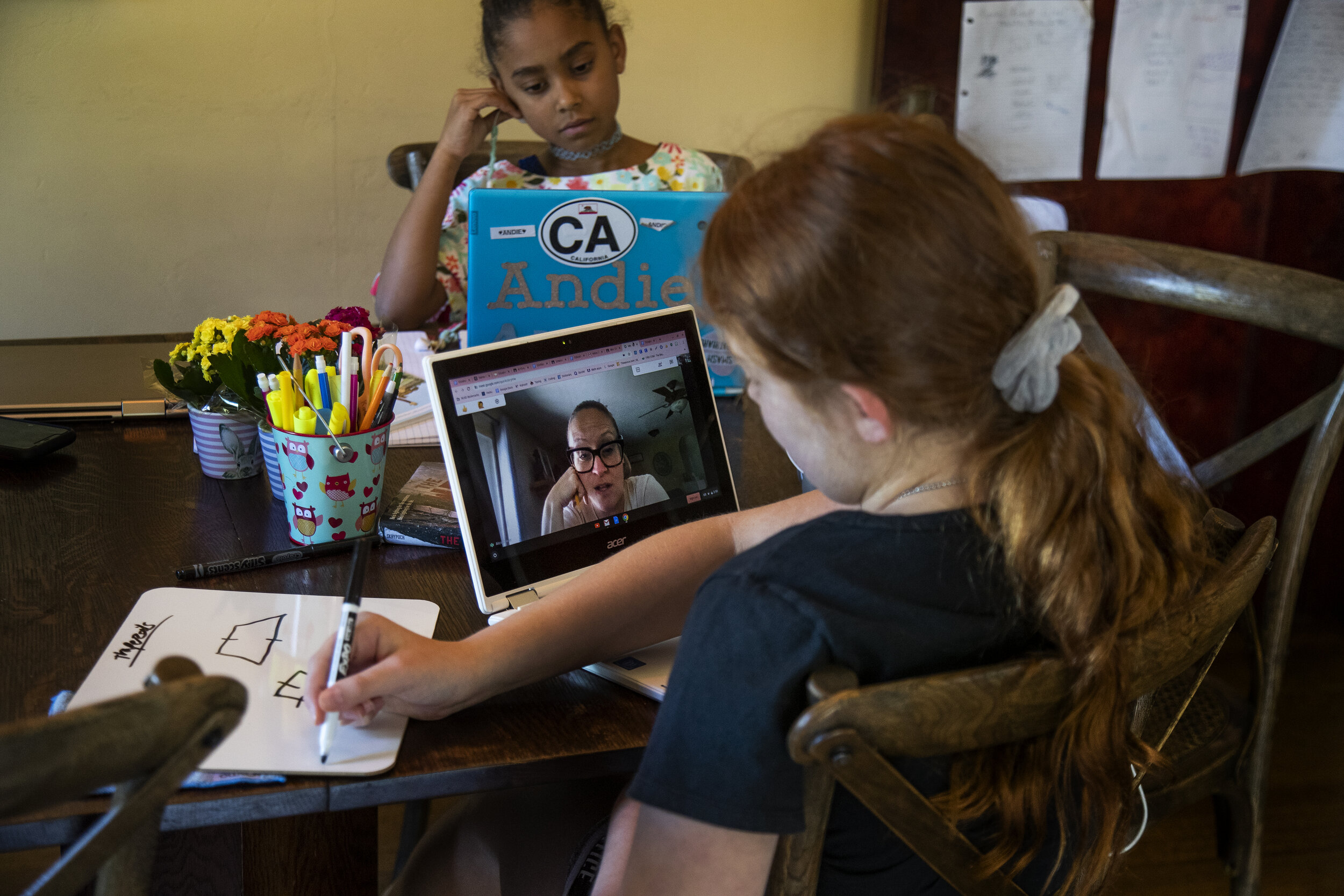  RIVERSIDE, CA- APRIL 16, 2020: Ellie Bristow, 11, checks in with her 5th grade teacher during a geometry class as her sister Andie, 6 works on a book report  at the kitchen table  in home schooling session during the coronavirus pandemic on April 16
