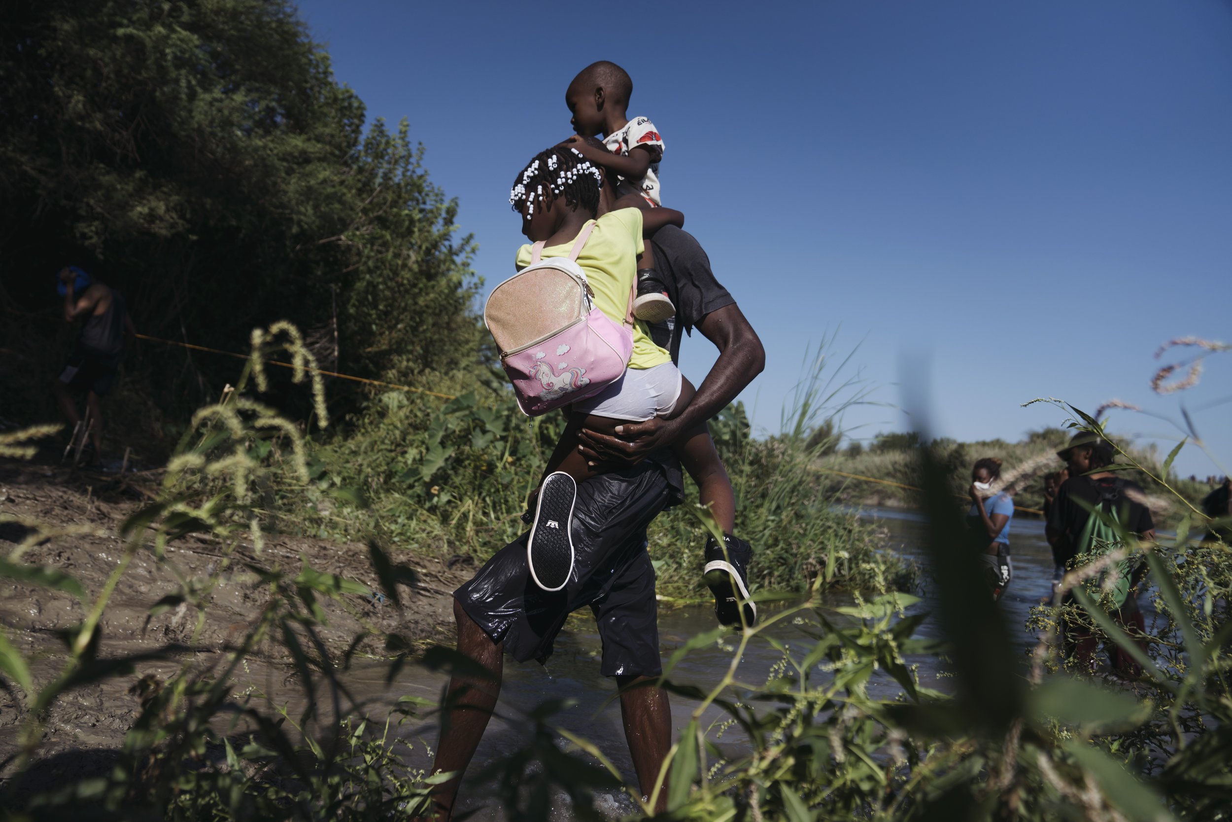 photo essay 2021 A man crosses onto the shore into Mexico carrying two children over the Rio Grande River near the Del Rio-Acuna Port of Entry in Acuna, Coahuila, Mexico, on Monday, Sept. 20, 2021.