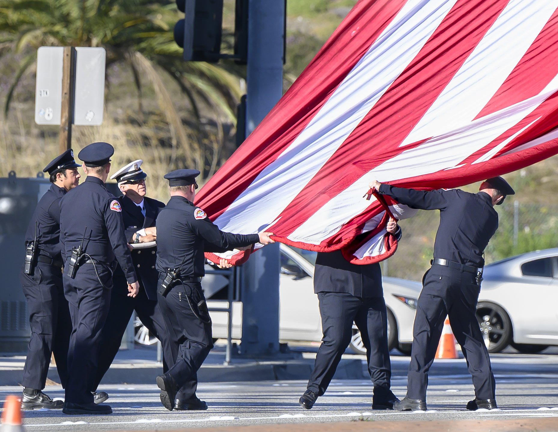  Fire fighters hustle to get control of a wind-whipped flag before the funeral procession for Huntington Beach Police Officer Nicholas Vella in Anaheim on Tuesday, March 8, 2022. Vella died in a helicopter crash Feb. 19 off the waters in Newport Beac