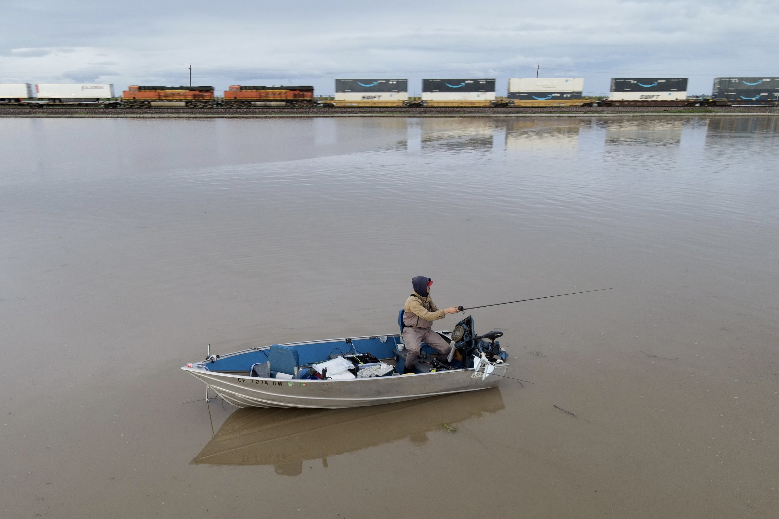  A man fishes in the floodwaters as a train passes after days of heavy rain in Corcoran, California, U.S., March 29, 2023.   