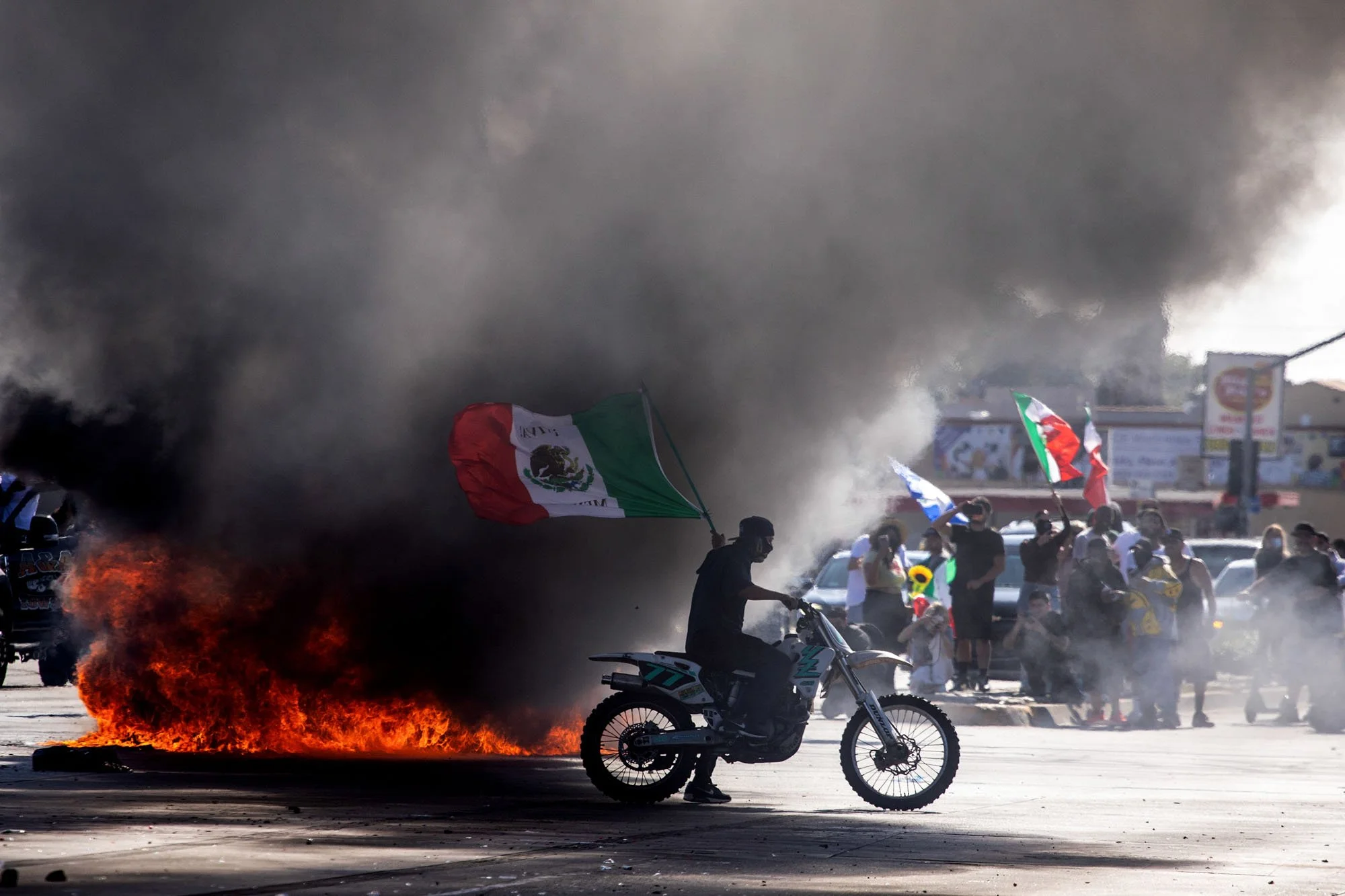  A demonstrator on a motorcycle waves a Mexican flag in front of a burning vehicle during a demonstration following federal immigration operations in the Compton neighborhood of Los Angeles on June 7, 2025. The protest erupted after Immigration and C