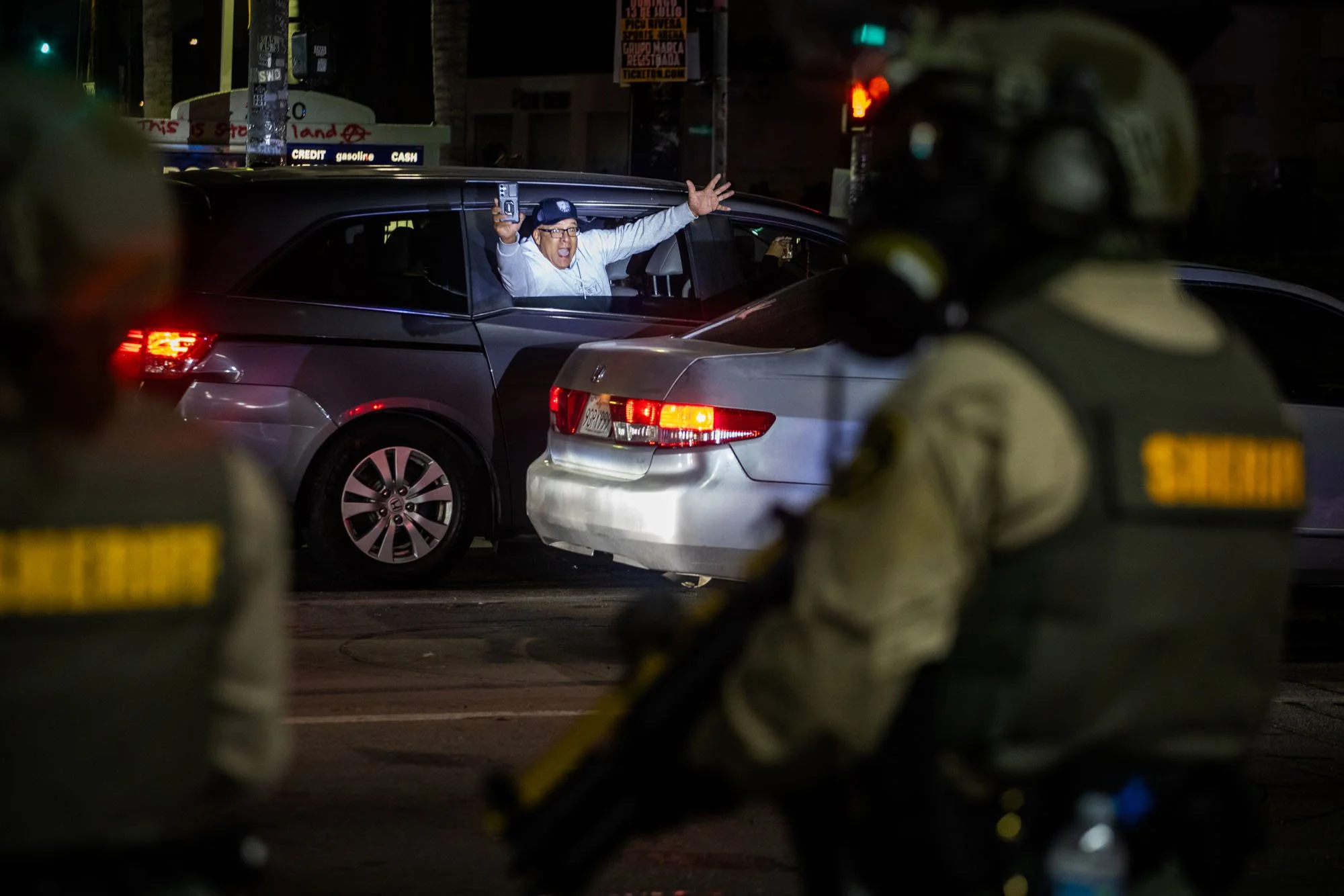  A man yells at law enforcement officers from his car window as Los Angeles County sheriff’s deputies stand nearby during a nighttime demonstration following federal immigration operations in the Compton neighborhood of Los Angeles on June 7, 2025. T
