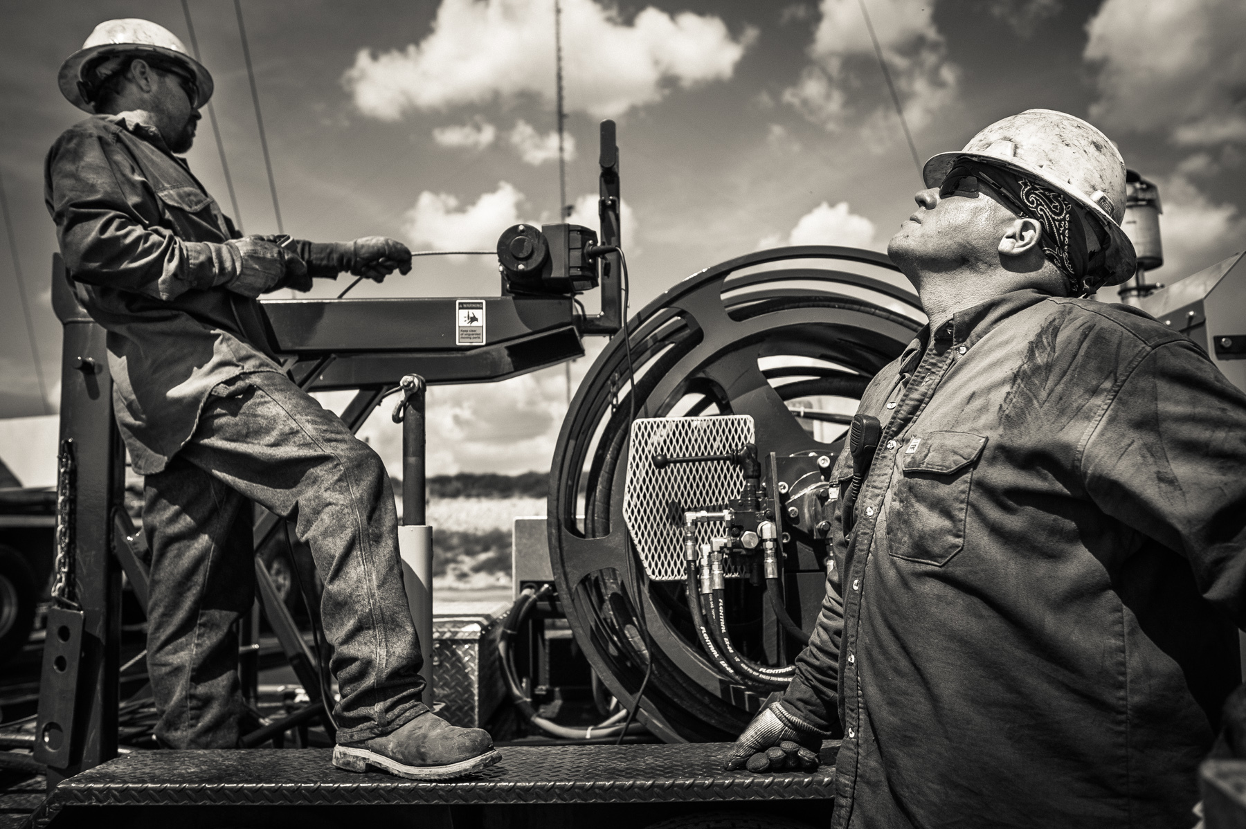 Men from a workover crew lifting a swivel head into place to complete the fracking of an oil well. Crews work in alternating 12 hour shifts throughout the entire drilling and fracking process. The work never stops on a drill site. 