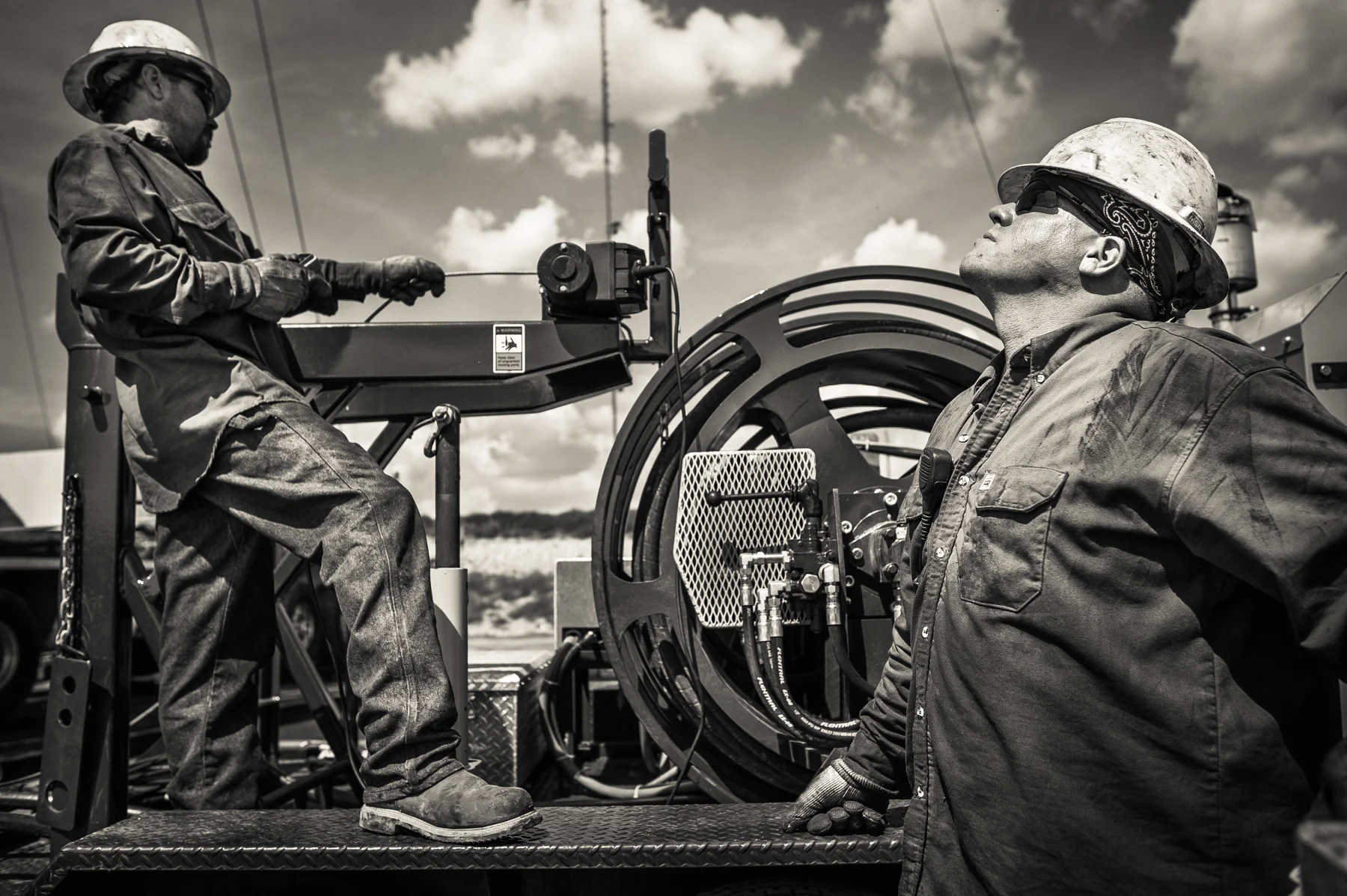 Men from a workover crew lifting a swivel head into place to complete the fracking of an oil well. Crews work in alternating 12 hour shifts throughout the entire drilling and fracking process. The work never stops on a drill site.