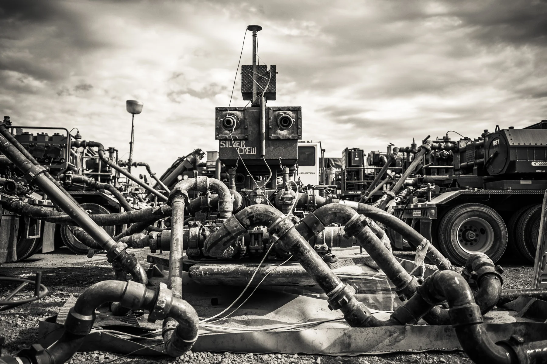 An oil well head during the process of Hydraulic Fracturing, aka fracking. The many pipes leading into the well contain water, sand and some chemical lubricants forced in by the massive pump trucks in the background. 